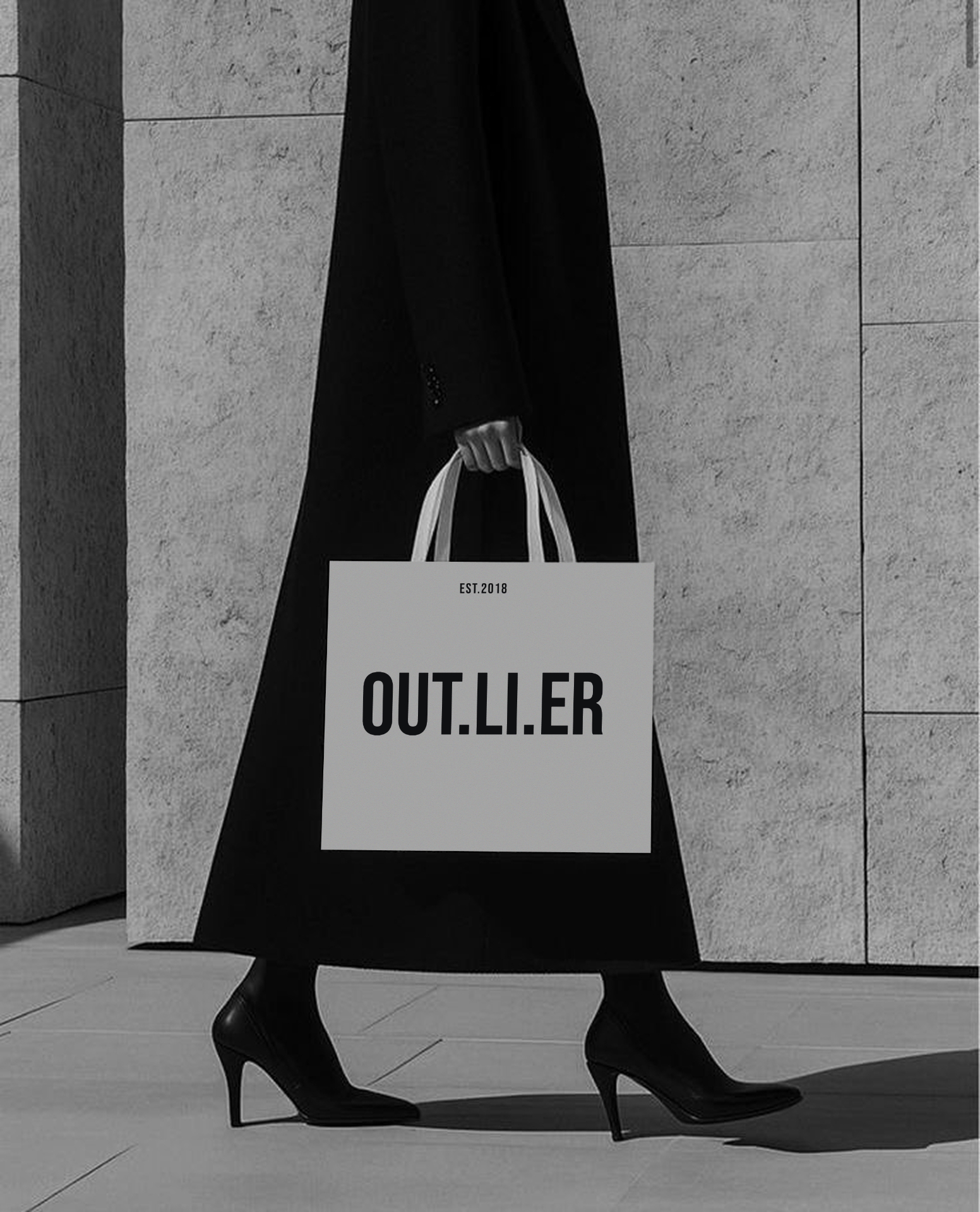 OUT.LI.ER tote bag carried in a tailored black coat